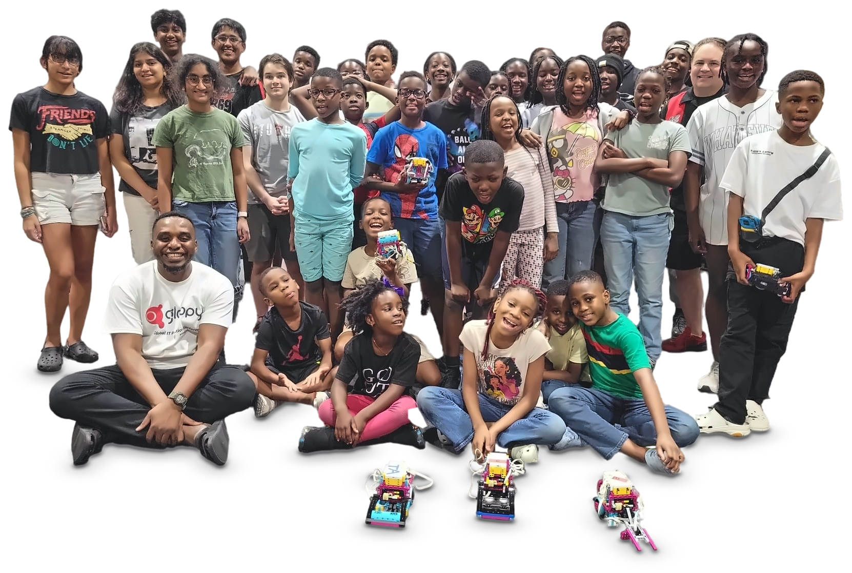 A big group of kids and mentors pose with the robots they built, three robots on the floor in front